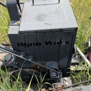 IMG_8841 - Montana Auctions by Kevin Hill Weathered gray metal toolbox mounted on farming equipment in tall grass; lid closed and handle on top with visible rust and stains.