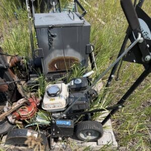 IMG_8842 - Montana Auctions by Kevin Hill Older industrial generator/pump sitting on a wooden pallet, overgrown with tall grass in an outdoor field.
