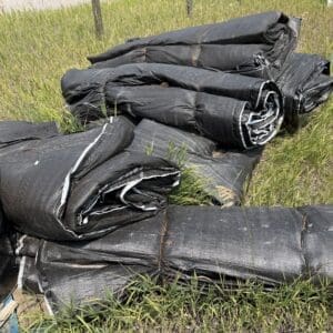 IMG_8844 - Montana Auctions by Kevin Hill Rolled black landscaping fabric sheets piled in a grassy field.
