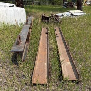 IMG_8846 - Montana Auctions by Kevin Hill Rusty metal rails and beams laid on overgrown grass in an outdoor junk yard.