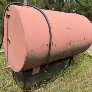 IMG_8857 - Montana Auctions by Kevin Hill Old pink horizontal storage tank on metal legs, outdoors, with hoses and moss along the bottom edge.