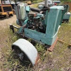IMG_8866 - Montana Auctions by Kevin Hill Old teal diesel generator on a rusting trailer in a grassy junkyard field, with other equipment in the background.