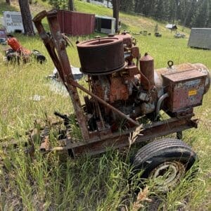 IMG_8867 - Montana Auctions by Kevin Hill Rusty old tractor surrounded by tall grass in a rural junkyard, with trailers and shipping containers in the background.