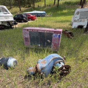 IMG_8876 - Montana Auctions by Kevin Hill Abandoned diesel generator in a grassy field with a rusted blue unit and a detached motor nearby; campers and caravans in the background.