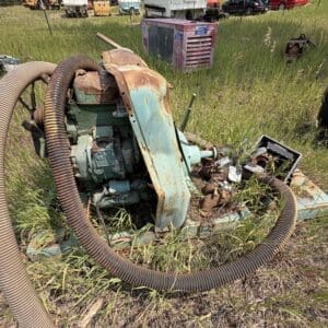 IMG_8877 - Montana Auctions by Kevin Hill Rusty green industrial pump with a large hose, sitting in tall grass in a yard; boats and cars visible in the background.