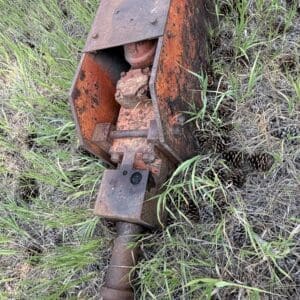IMG_8879 - Montana Auctions by Kevin Hill Rusty orange industrial tool attachment lying in tall grass, with a black hose draped over it.