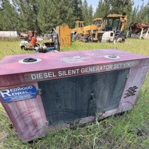 IMG_8880 - Montana Auctions by Kevin Hill Red diesel silent generator set in a grassy outdoor lot with orange construction machinery in the background; labeled 'DIESEL SILENT GENERATOR SET 17KW' on a pink cabinet.