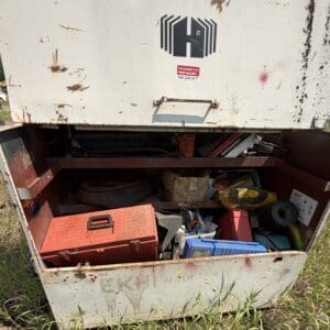 IMG_8885 - Montana Auctions by Kevin Hill Open metal tool chest filled with various tools and boxes on a grassy outdoor area, rusty and dusty with a red toolbox on top.