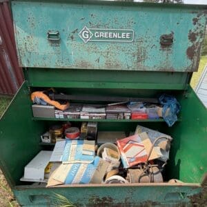 IMG_8889 - Montana Auctions by Kevin Hill Open green dumpster filled with assorted junk, including cardboard boxes, tools, and metal parts, outdoors with rust marks around the edges.