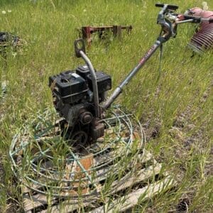 IMG_8905 - Montana Auctions by Kevin Hill Gas-powered garden tiller in a grassy field showing the engine and handlebars.