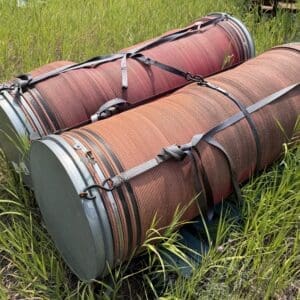 IMG_8906 - Montana Auctions by Kevin Hill Two large red-orange industrial hoses coiled and strapped together in tall grass outdoors.