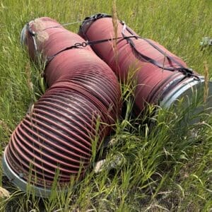 IMG_8907 - Montana Auctions by Kevin Hill Two large red corrugated drainage pipes secured with straps lying in tall grass in an open field.