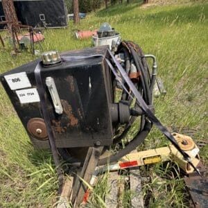 IMG_8913 - Montana Auctions by Kevin Hill Rusty black industrial machine on a trailer in a grassy field, with hoses and straps coiled around it.