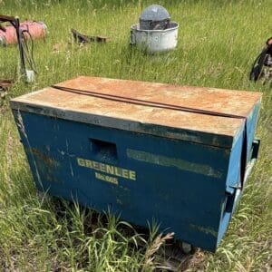 IMG_8915 - Montana Auctions by Kevin Hill Rusty blue metal toolbox on a wheeled cart in a grassy field, labeled GREENLEE No. 665 with a rusted orange lid.
