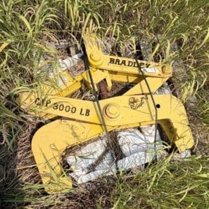 IMG_8924 - Montana Auctions by Kevin Hill Yellow industrial lifting clamp/tripod lying in tall grass, stamped with 'BRADLEY' and '8000 LB' on its frame.