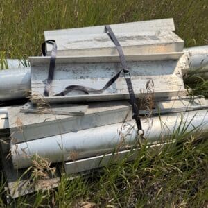 IMG_8928 - Montana Auctions by Kevin Hill Stack of metal panels and pipes tied with straps resting in tall grass beside a pipe line.