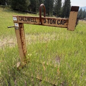 IMG_8933 - Montana Auctions by Kevin Hill Rusty metal support bar labeled Caldwell 3-ton cap in a grassy field with trees in the background