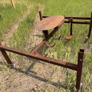 IMG_8935 - Montana Auctions by Kevin Hill Rusty metal agricultural frame with hooks and a small platform, lying in a field of tall grass; appears to be an old planter or cultivator.
