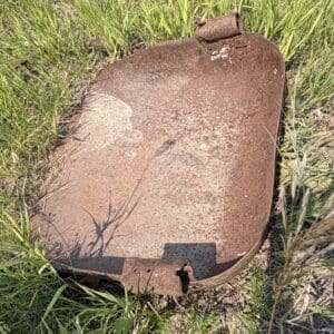 IMG_8940 - Montana Auctions by Kevin Hill Rusty curved metal hatch with hinges lying in a grassy field, sunlit and weathered.