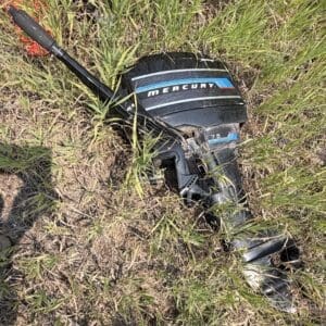 IMG_8943 - Montana Auctions by Kevin Hill Damaged Mercury 75 outboard motor lying in tall grass after an incident by the shoreline/field area.