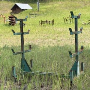 IMG_8951 - Montana Auctions by Kevin Hill Two rusty green metal farming racks stand in a grassy field with a small shed in the background.