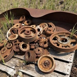 IMG_8969 - Montana Auctions by Kevin Hill Pile of rusted metal pulleys and wheels on a weathered wooden pallet in a grassy field outdoors.