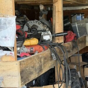 IMG_8982 - Montana Auctions by Kevin Hill Cluttered wooden shelf with power tools (circular saw, drill) and tangled cords in a workshop/garage storage area.