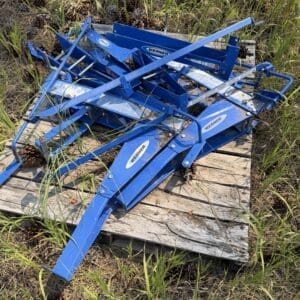 IMG_8984 - Montana Auctions by Kevin Hill Blue metal farming implement pieces piled on a weathered wooden pallet in a grassy area (likely a harrow/c tillage attachment). It’s branded Werner/Werner.